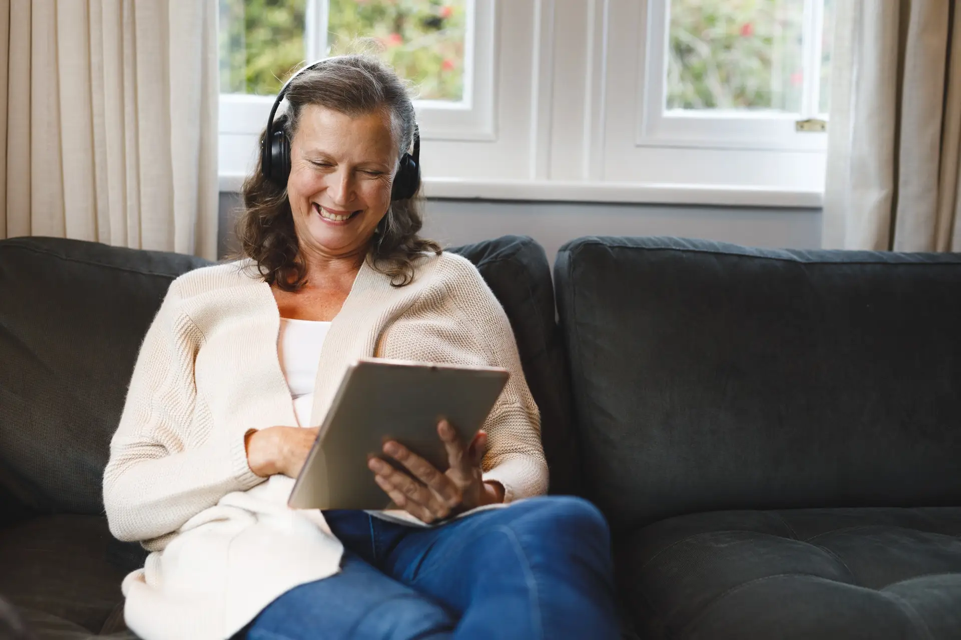 happy-senior-caucasian-woman-in-living-room-sitting-on-sofa-wearing-headphones-using-tablet.jpg